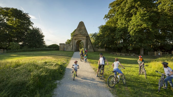 A family cycling along a path in parkland at Nostell, Yorkshire